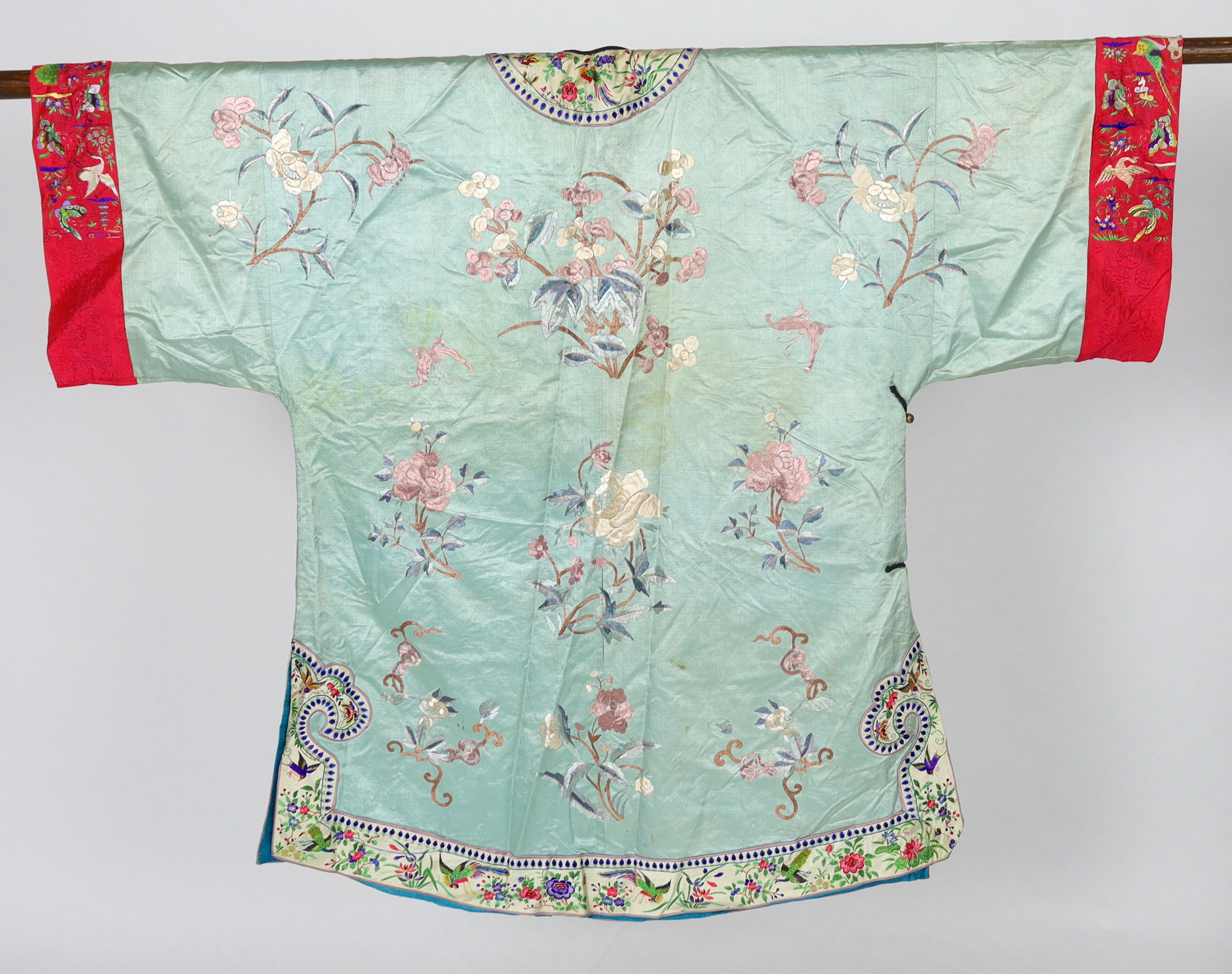 An early 20th century Chinese silk embroidered turquoise robe, embroidered in pastel silk with butterflies and flowers all over, polychrome embroidered braiding edged with lilac and bright pink sleeve bands embroidered w